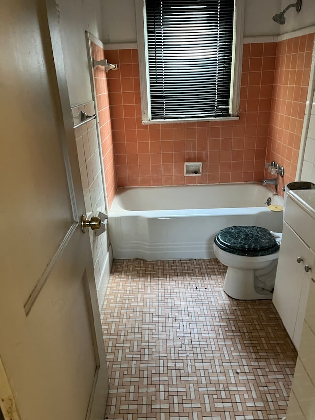 full bathroom with tiled shower / bath combo, toilet, tile walls, and vanity