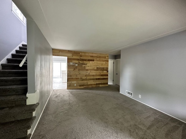 unfurnished living room featuring dark carpet and wooden walls