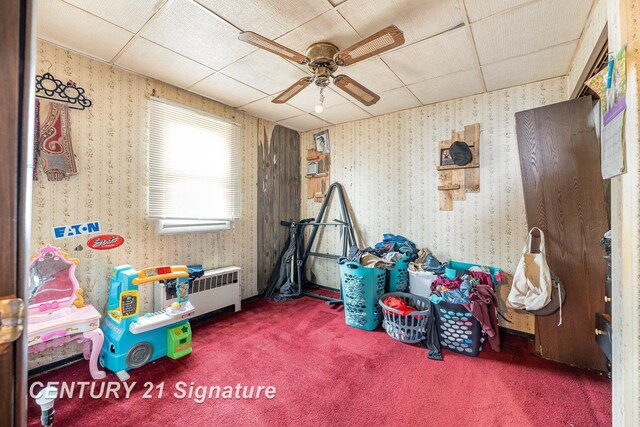 playroom with ceiling fan, a paneled ceiling, radiator heating unit, and carpet