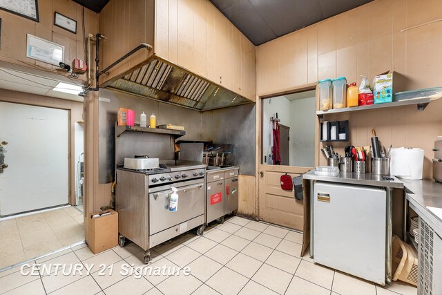 kitchen featuring fridge, high end stainless steel range, light tile patterned flooring, and wood walls