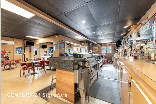 kitchen with an AC wall unit, a breakfast bar area, and a drop ceiling