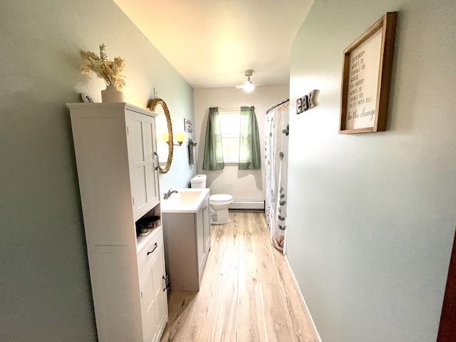 bathroom with a baseboard heating unit, hardwood / wood-style floors, vanity, curtained shower, and toilet