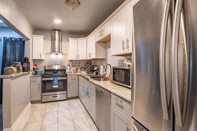 kitchen with appliances with stainless steel finishes, sink, white cabinets, light stone counters, and wall chimney range hood