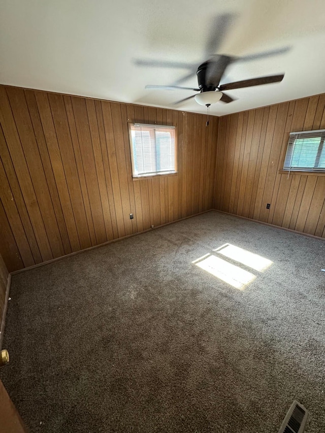 empty room with wooden walls, carpet floors, and ceiling fan