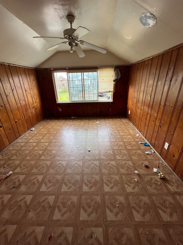 interior space with light parquet flooring, vaulted ceiling, ceiling fan, and wooden walls