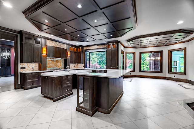 kitchen with tasteful backsplash, dark brown cabinetry, a kitchen island with sink, and coffered ceiling