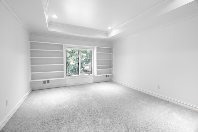 empty room featuring carpet flooring, built in shelves, a tray ceiling, and crown molding