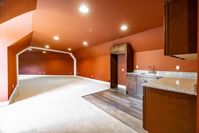 kitchen with lofted ceiling, sink, light stone countertops, a textured ceiling, and light colored carpet