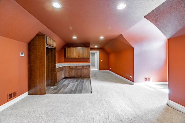 bonus room featuring a textured ceiling, lofted ceiling, and light carpet