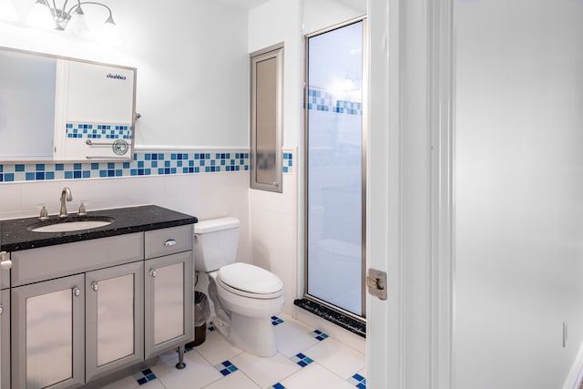 bathroom featuring walk in shower, tile patterned flooring, toilet, vanity, and tile walls