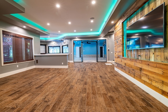 unfurnished living room with a tray ceiling, wooden walls, and hardwood / wood-style flooring