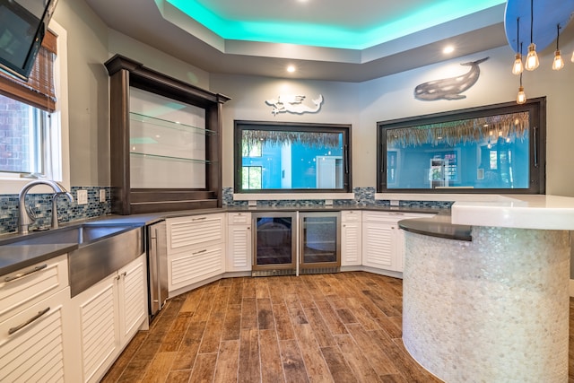 bar featuring a tray ceiling, dark wood-type flooring, sink, white cabinetry, and hanging light fixtures