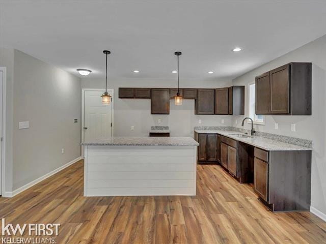 kitchen with pendant lighting, sink, a center island, light stone counters, and light wood-type flooring