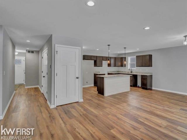 kitchen featuring dark brown cabinetry, a kitchen island, hanging light fixtures, and light hardwood / wood-style flooring