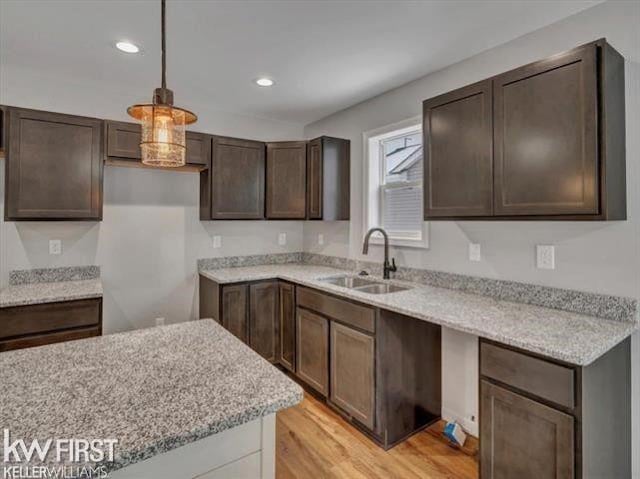 kitchen featuring dark brown cabinetry, decorative light fixtures, sink, and light wood-type flooring