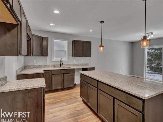 kitchen with sink, light hardwood / wood-style flooring, hanging light fixtures, dark brown cabinetry, and light stone countertops