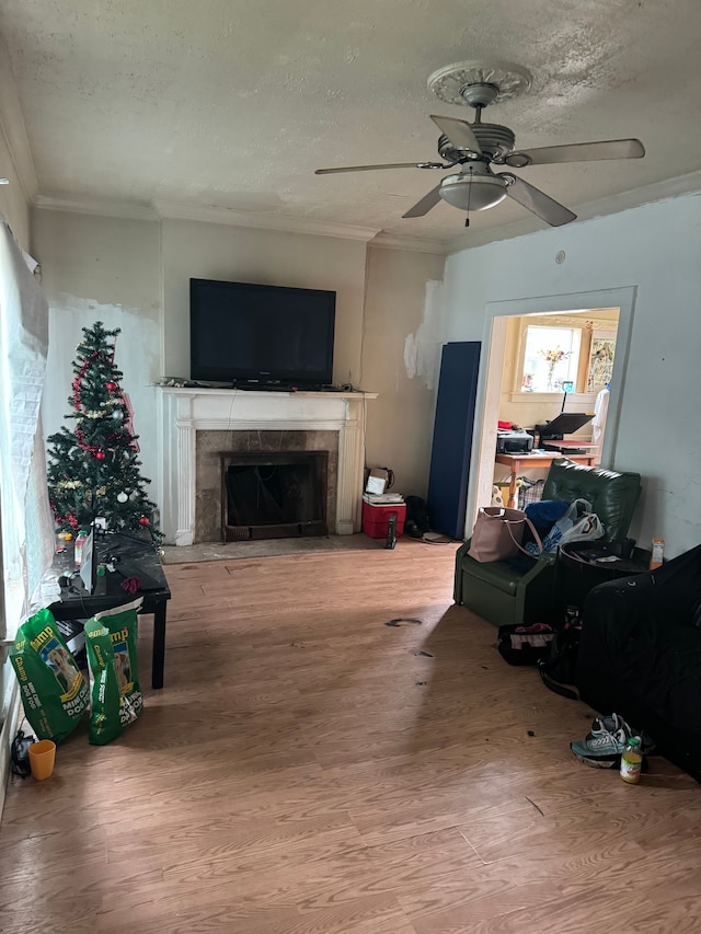 living room with ceiling fan, crown molding, hardwood / wood-style floors, a textured ceiling, and a tiled fireplace