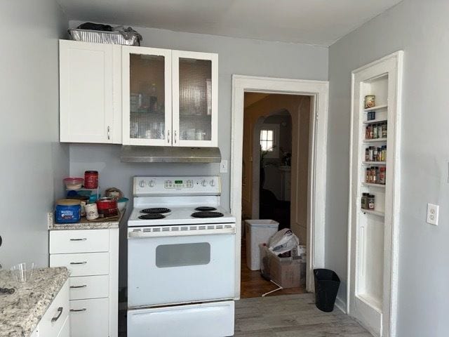 kitchen featuring light stone countertops, white cabinets, wood-type flooring, and white electric range