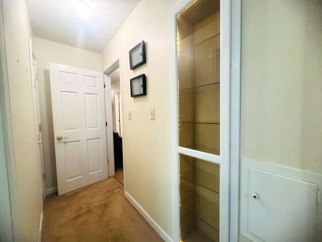 corridor with a textured ceiling and light colored carpet