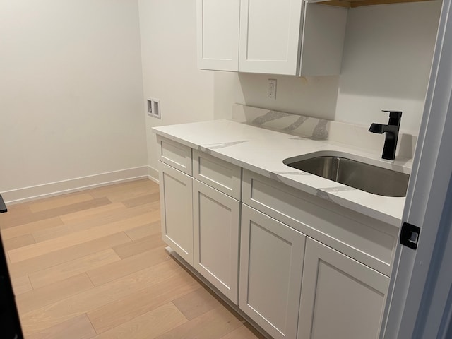 kitchen featuring light stone counters, sink, white cabinetry, and light hardwood / wood-style flooring