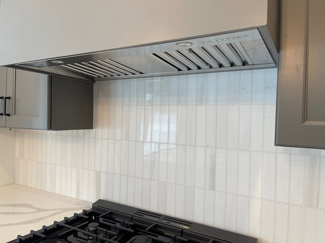 interior details with backsplash, gray cabinets, stovetop, and wall chimney exhaust hood