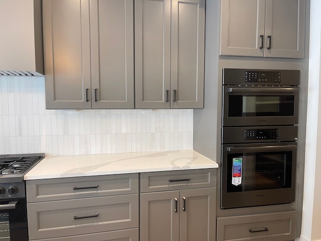 kitchen with stainless steel double oven, gray cabinets, gas stove, and wall chimney range hood