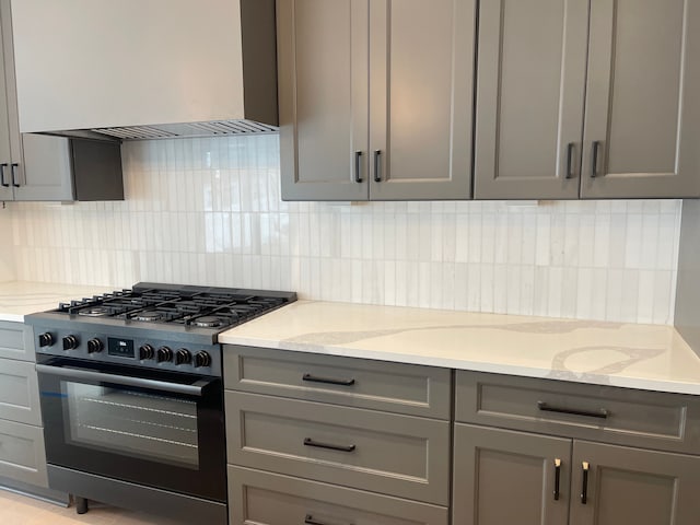 kitchen featuring gray cabinetry, range with gas cooktop, light stone countertops, and custom exhaust hood