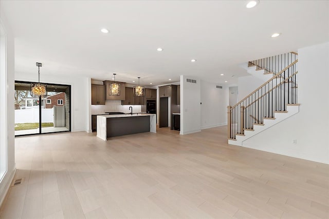 kitchen with hanging light fixtures, dark brown cabinets, a kitchen island with sink, and light wood-type flooring