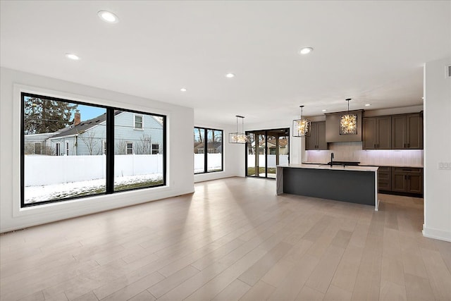 kitchen with tasteful backsplash, dark brown cabinets, a kitchen island with sink, and decorative light fixtures