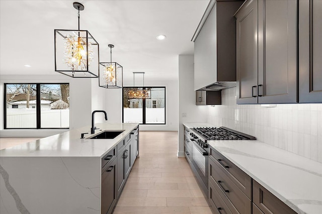 kitchen with sink, stainless steel stove, light stone counters, and wall chimney exhaust hood