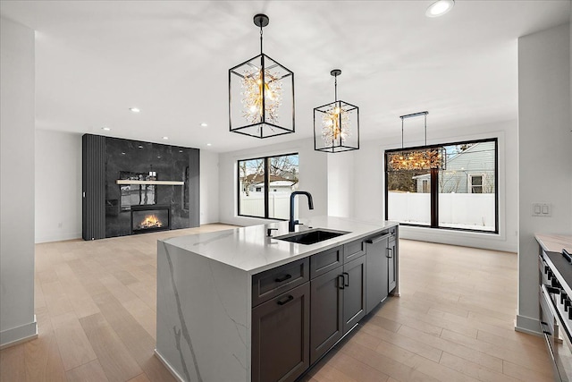 kitchen featuring sink, light stone counters, decorative light fixtures, a high end fireplace, and a kitchen island with sink