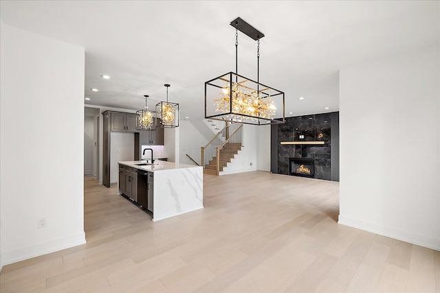 kitchen with sink, hanging light fixtures, dishwasher, a fireplace, and light stone countertops