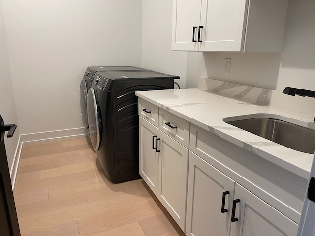 washroom featuring cabinets, sink, washing machine and clothes dryer, and light hardwood / wood-style floors