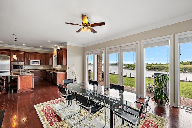 dining area with dark hardwood / wood-style floors, ceiling fan, a water view, and crown molding