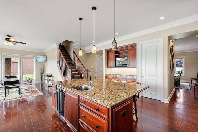 kitchen with light stone countertops, sink, hanging light fixtures, dark hardwood / wood-style floors, and a kitchen island with sink