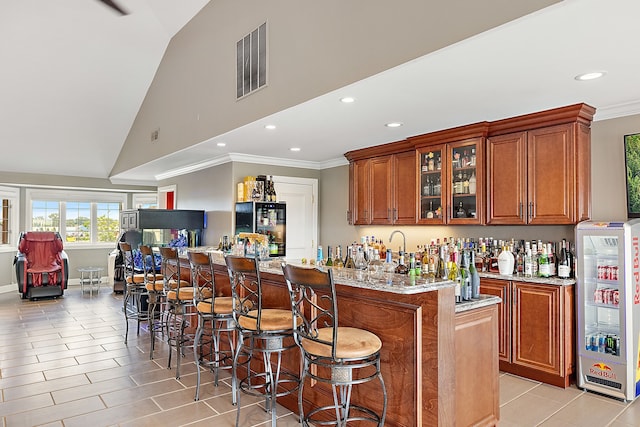 bar featuring light stone counters, ornamental molding, beverage cooler, and vaulted ceiling