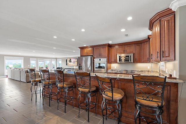 kitchen featuring a kitchen bar, sink, light stone countertops, and stainless steel appliances