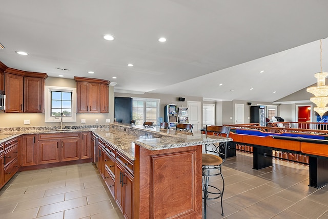 kitchen with sink, hanging light fixtures, a kitchen breakfast bar, light stone counters, and kitchen peninsula