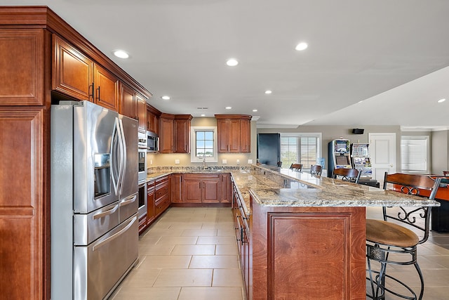 kitchen featuring a kitchen breakfast bar, sink, light stone countertops, appliances with stainless steel finishes, and kitchen peninsula