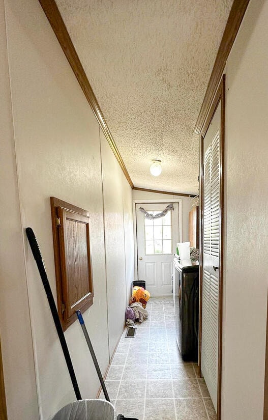 hall with a textured ceiling, washing machine and dryer, and ornamental molding