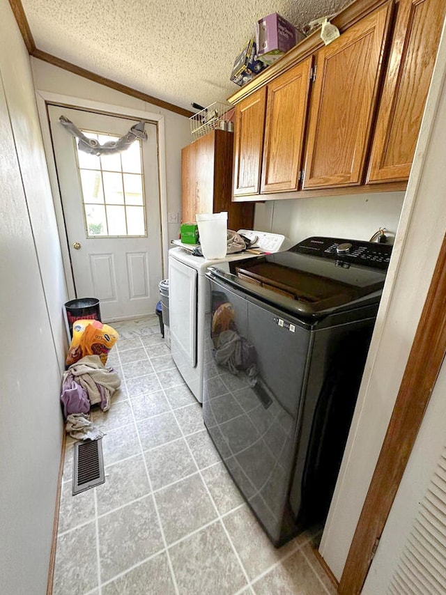 clothes washing area featuring separate washer and dryer, light tile patterned flooring, cabinets, and a textured ceiling