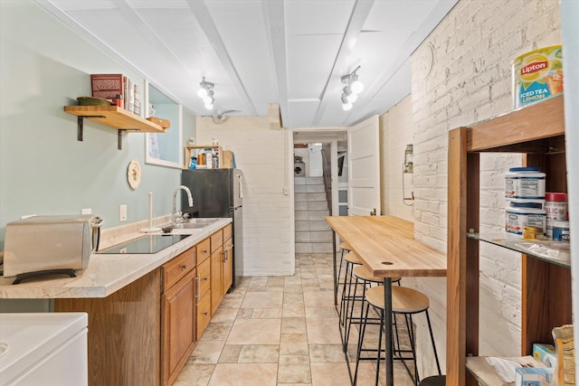 kitchen with sink, a kitchen breakfast bar, beamed ceiling, brick wall, and black electric stovetop