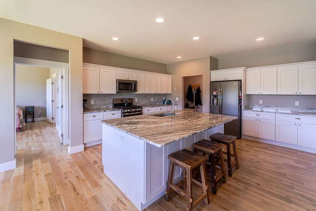 kitchen featuring white cabinets, light hardwood / wood-style floors, an island with sink, and appliances with stainless steel finishes