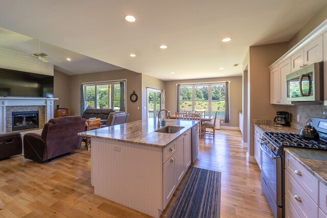 829 N Van Dyke Rd, Imlay City, MI 48444 - kitchen featuring stainless steel appliances, a sink, a stone fireplace, light wood-style floors, and a kitchen island with sink