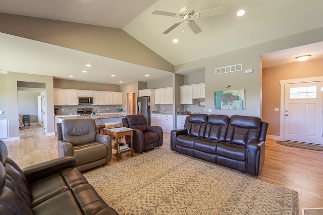 living room with ceiling fan, sink, high vaulted ceiling, and light hardwood / wood-style flooring