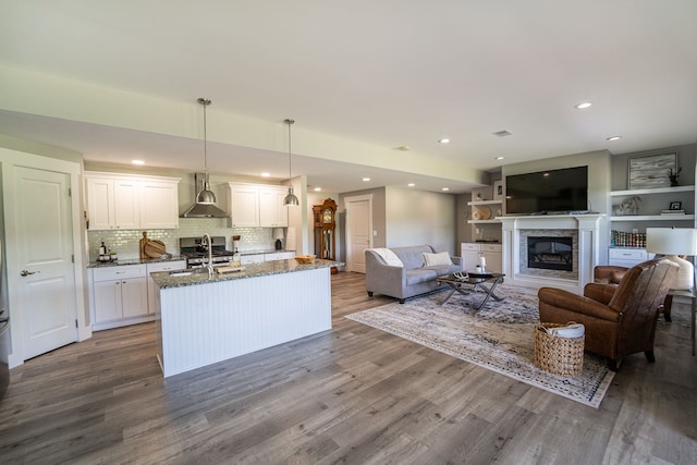 kitchen with dark stone counters, wall chimney range hood, white cabinets, hardwood / wood-style floors, and hanging light fixtures