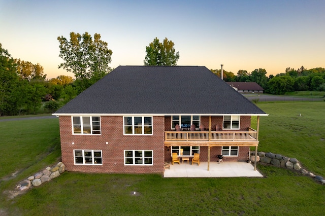 back house at dusk featuring a patio, a wooden deck, and a lawn