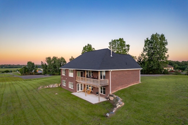 back house at dusk featuring a lawn, a patio area, and a balcony