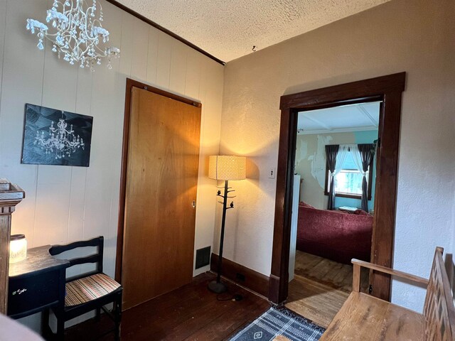 hall with hardwood / wood-style flooring, a notable chandelier, a textured ceiling, wooden walls, and ornamental molding