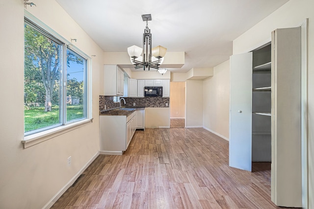 kitchen featuring hanging light fixtures, an inviting chandelier, light hardwood / wood-style floors, decorative backsplash, and white cabinets